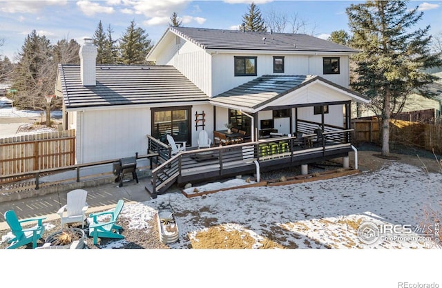 snow covered property featuring a fire pit, a fenced backyard, a chimney, a tiled roof, and a deck