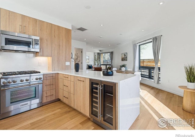 kitchen with light brown cabinets, stainless steel appliances, wine cooler, kitchen peninsula, and light wood-type flooring