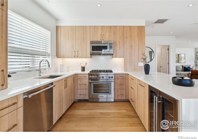 kitchen with light brown cabinetry, sink, beverage cooler, and stainless steel appliances