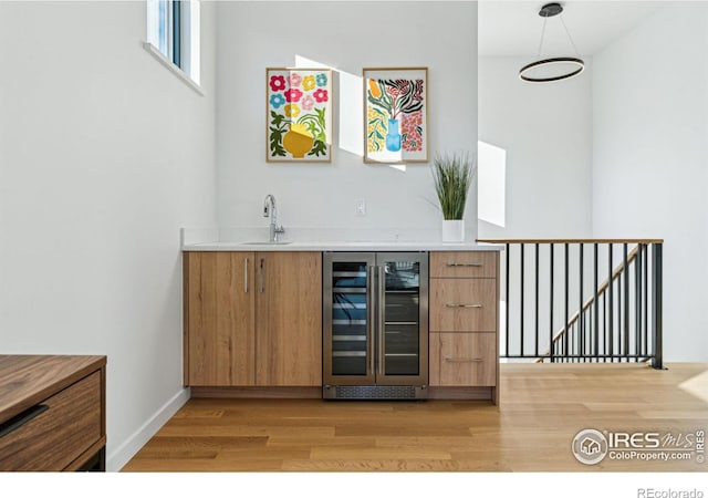 bar with decorative light fixtures, sink, light hardwood / wood-style flooring, and wine cooler