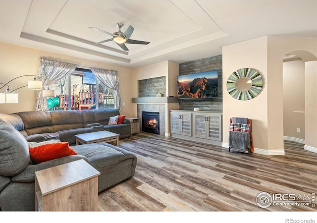 living room featuring ceiling fan, hardwood / wood-style floors, a tray ceiling, and a fireplace