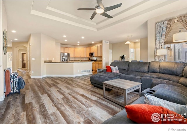 living room featuring ceiling fan, light hardwood / wood-style floors, and a tray ceiling