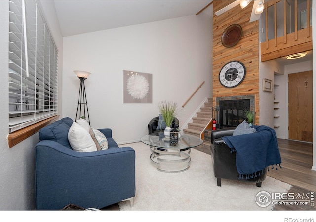 living room with ceiling fan, hardwood / wood-style floors, wooden walls, and high vaulted ceiling