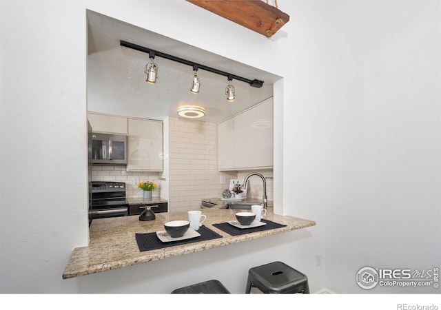 kitchen with white cabinets, light stone counters, decorative backsplash, range with electric stovetop, and sink