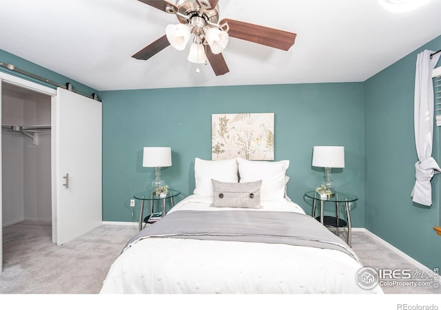 bedroom with a spacious closet, ceiling fan, a closet, a barn door, and light colored carpet