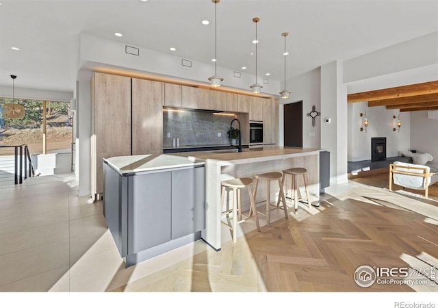 kitchen featuring black oven, tasteful backsplash, an island with sink, hanging light fixtures, and light parquet flooring