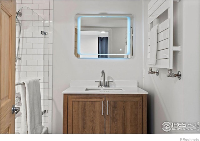 bathroom with tiled shower, vanity, and radiator heating unit