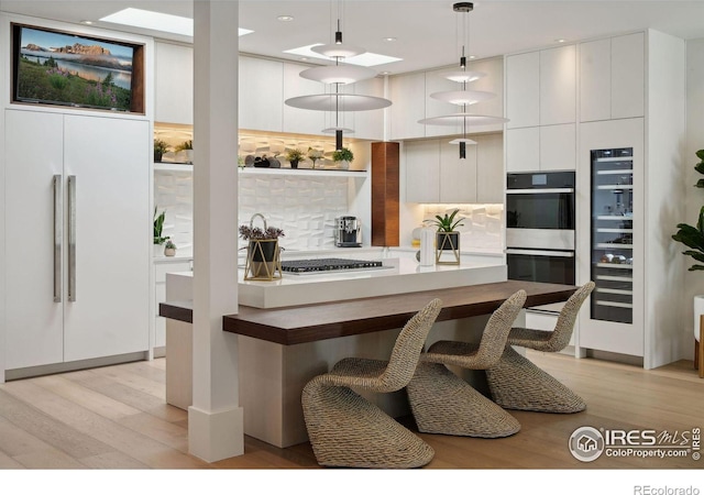 kitchen with pendant lighting, light hardwood / wood-style floors, tasteful backsplash, paneled refrigerator, and white cabinetry