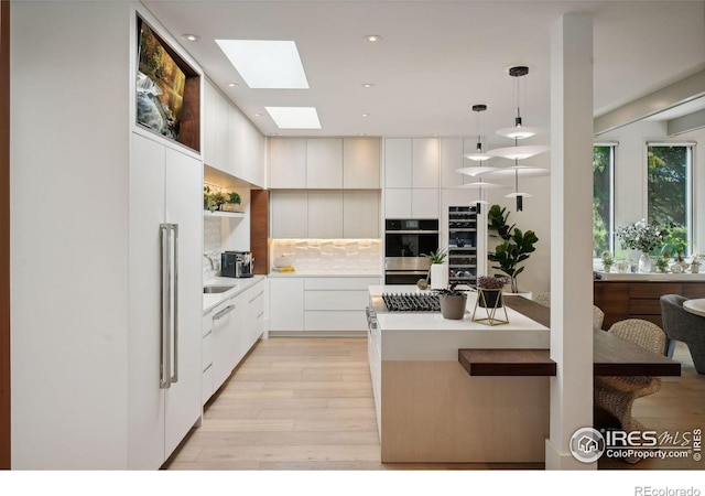 kitchen featuring white cabinetry, decorative backsplash, a skylight, stainless steel double oven, and pendant lighting