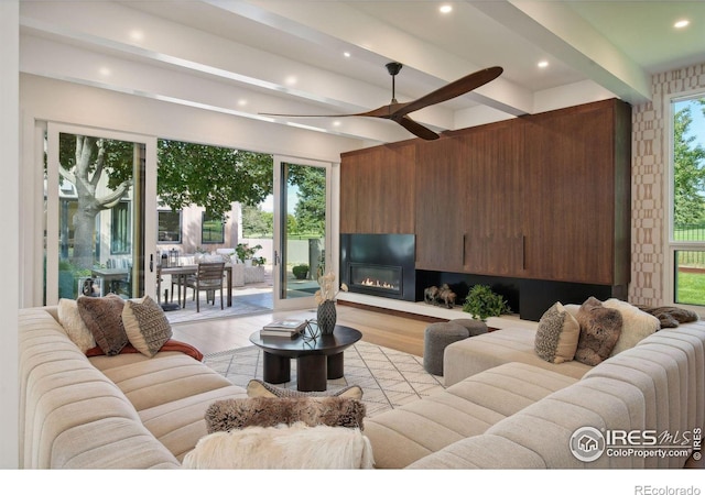 living room featuring ceiling fan, light wood-type flooring, and beamed ceiling