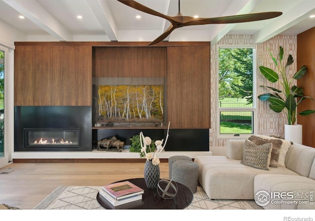 living room featuring a large fireplace, ceiling fan, light hardwood / wood-style flooring, and beamed ceiling