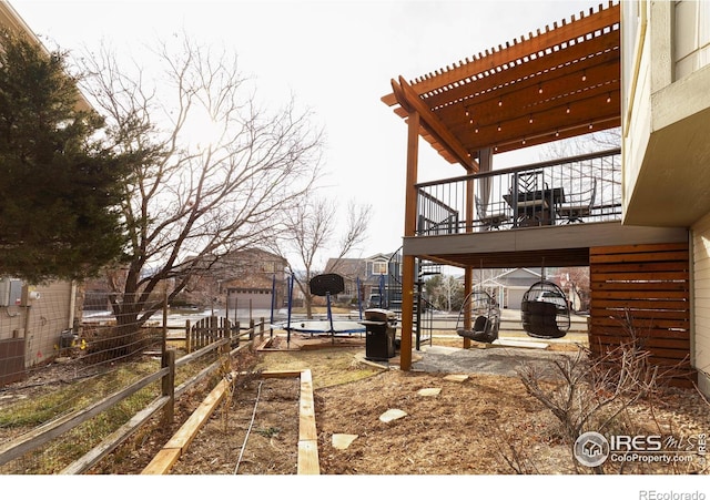 view of yard featuring a trampoline, fence, a wooden deck, stairs, and a pergola