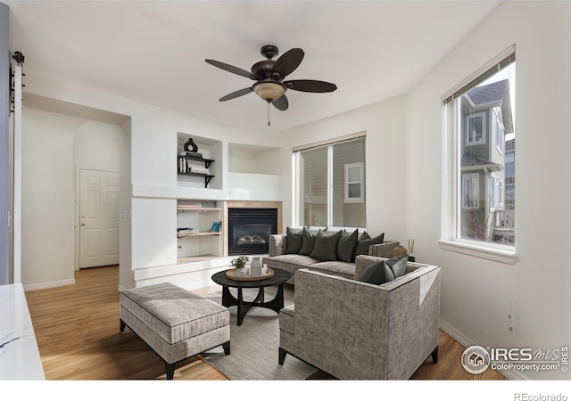 living area with a fireplace, baseboards, ceiling fan, and wood finished floors