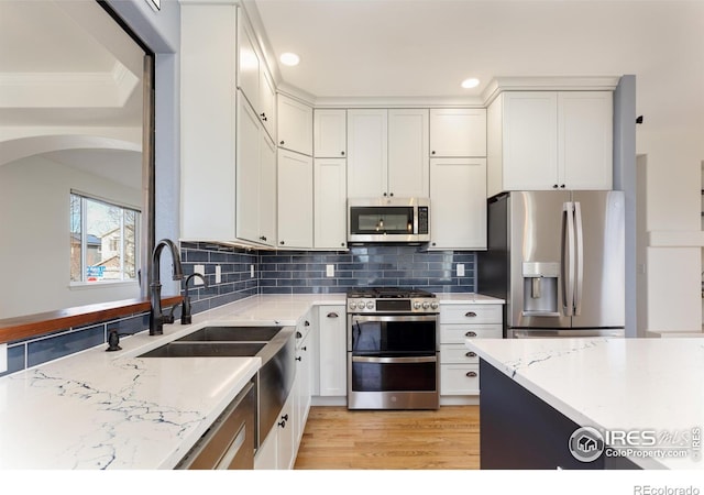 kitchen featuring white cabinetry, light stone countertops, arched walkways, and stainless steel appliances