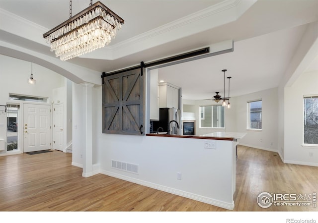 kitchen with light wood-type flooring, visible vents, a barn door, a peninsula, and white cabinets