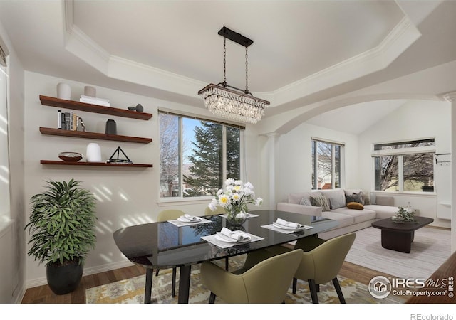 dining room with arched walkways, a raised ceiling, ornate columns, and wood finished floors