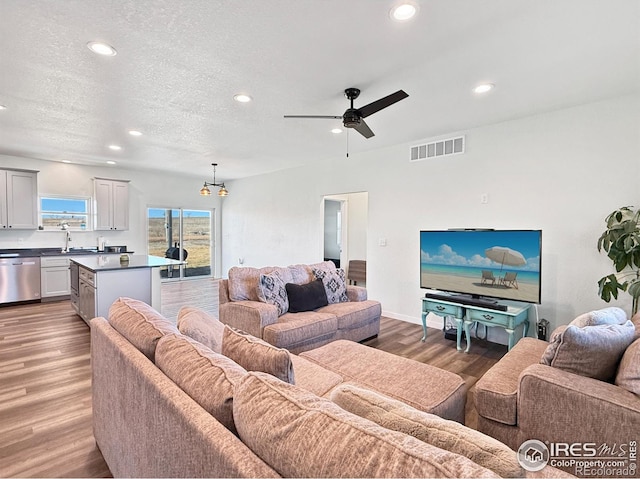 living room with ceiling fan with notable chandelier, sink, a textured ceiling, and hardwood / wood-style floors