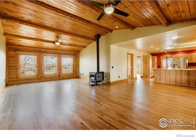 unfurnished living room featuring lofted ceiling with beams, wooden ceiling, a wood stove, ceiling fan, and light hardwood / wood-style floors