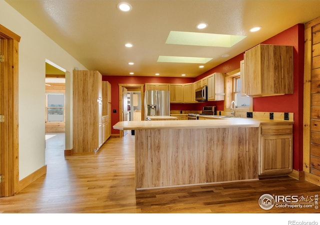 kitchen featuring a skylight, stainless steel appliances, light hardwood / wood-style floors, kitchen peninsula, and light brown cabinets