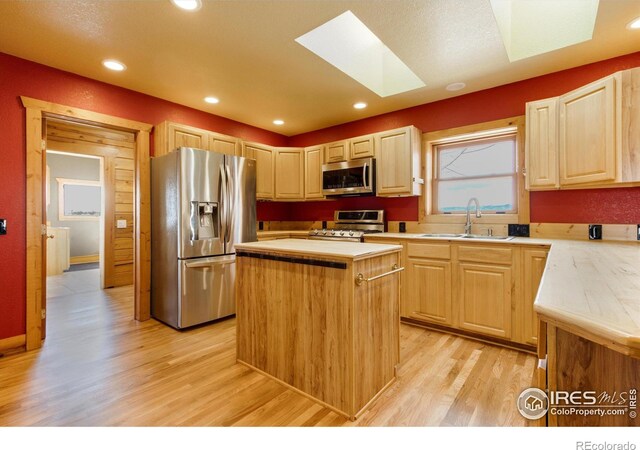 kitchen with sink, a skylight, a center island, appliances with stainless steel finishes, and light hardwood / wood-style floors