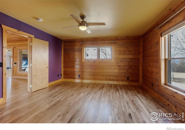 empty room with a healthy amount of sunlight, wooden walls, and light wood-type flooring