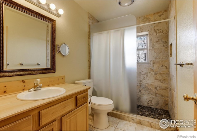 bathroom featuring a tile shower, vanity, tile patterned flooring, and toilet