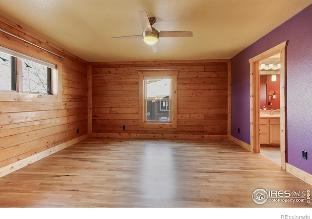 empty room with light hardwood / wood-style floors, a healthy amount of sunlight, and wood walls