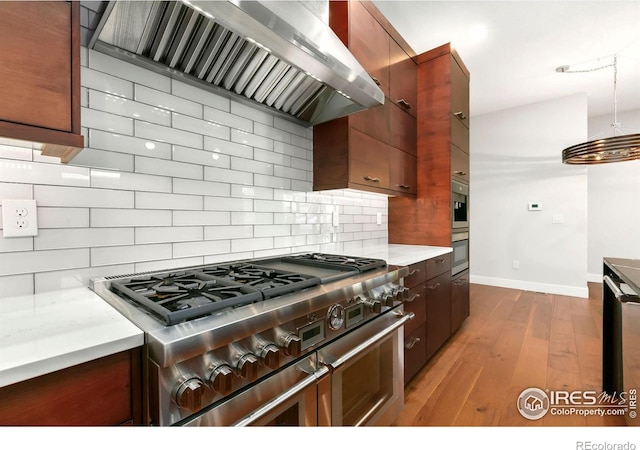 kitchen with range with two ovens, wall chimney exhaust hood, decorative light fixtures, decorative backsplash, and light wood-type flooring