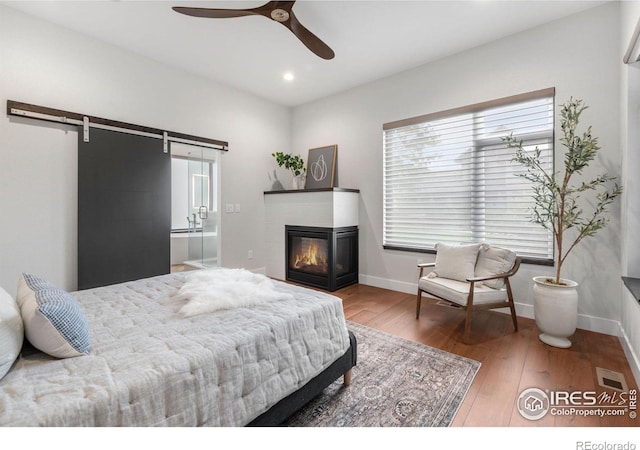 bedroom with ceiling fan, a barn door, and wood-type flooring