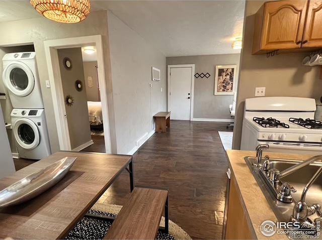 kitchen featuring sink, stacked washer / drying machine, and dark wood-type flooring