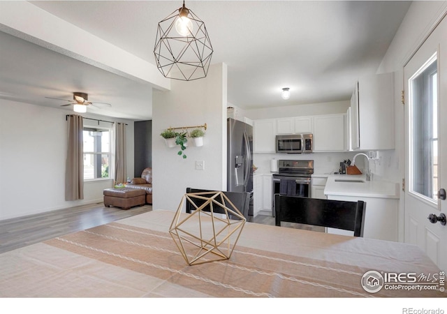 kitchen with stainless steel appliances, sink, white cabinetry, light wood-type flooring, and hanging light fixtures