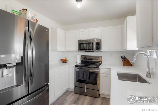 kitchen with stainless steel appliances, light wood-type flooring, light stone counters, sink, and white cabinetry