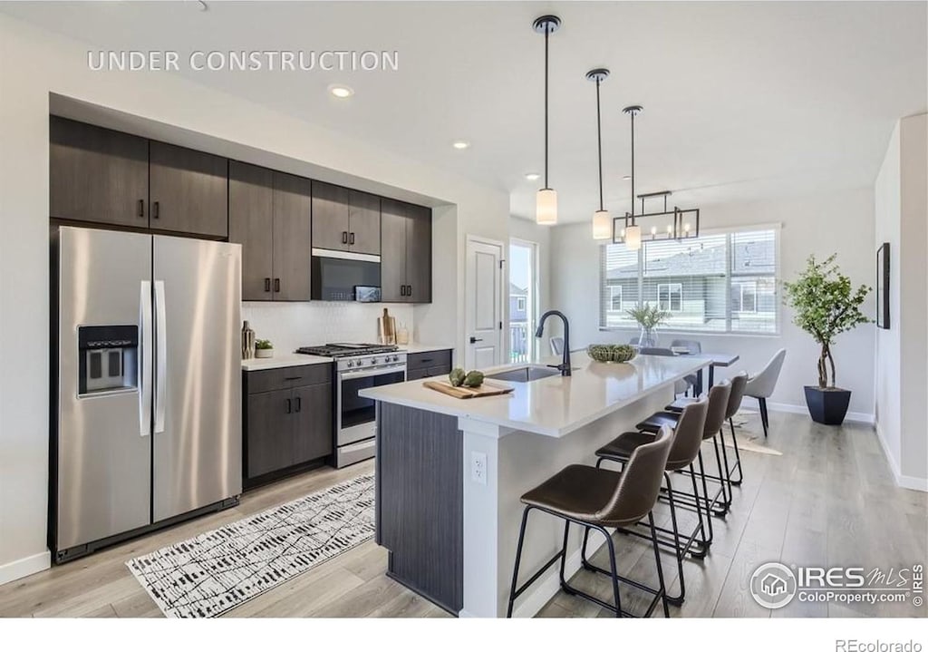 kitchen with dark brown cabinetry, sink, an island with sink, stainless steel appliances, and light hardwood / wood-style floors