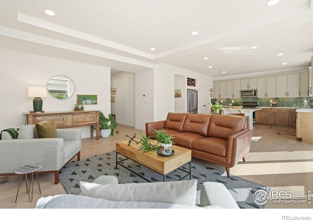 living room with light wood-type flooring and a raised ceiling