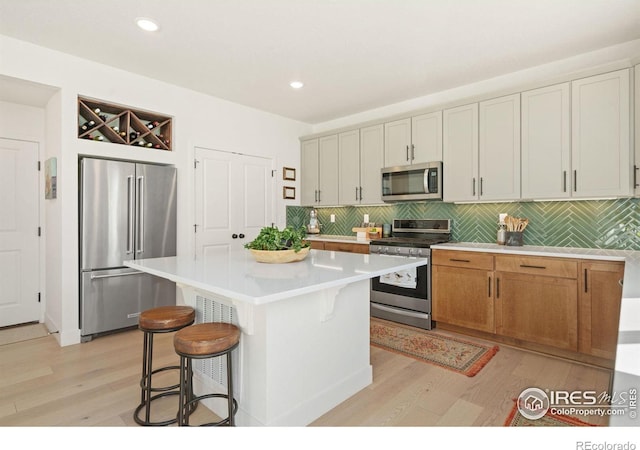 kitchen with tasteful backsplash, a kitchen bar, a kitchen island, light wood-type flooring, and appliances with stainless steel finishes