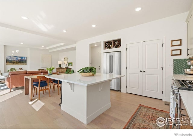 kitchen with appliances with stainless steel finishes, light hardwood / wood-style floors, a kitchen bar, a kitchen island, and white cabinetry