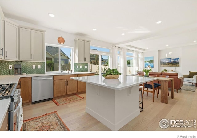 kitchen featuring stainless steel appliances, sink, light hardwood / wood-style floors, a kitchen island, and a breakfast bar