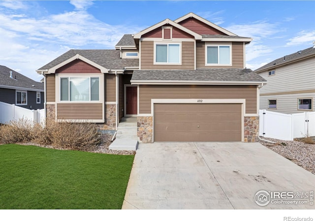 craftsman-style home featuring a shingled roof, fence, stone siding, driveway, and a front lawn