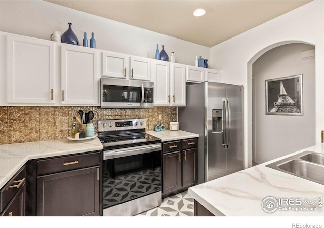 kitchen featuring stainless steel appliances, light stone counters, decorative backsplash, white cabinets, and sink