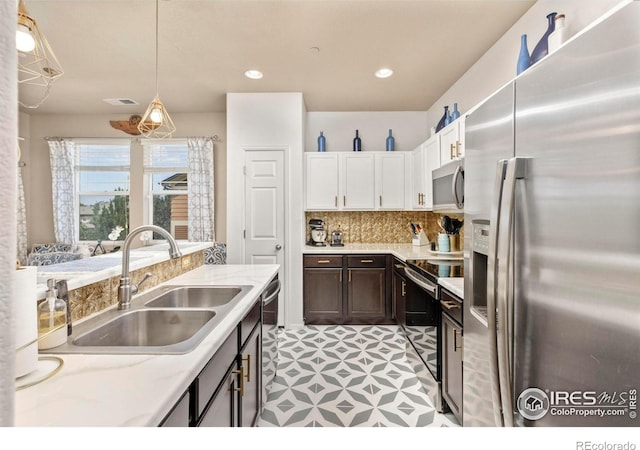 kitchen with stainless steel appliances, white cabinets, decorative light fixtures, backsplash, and sink