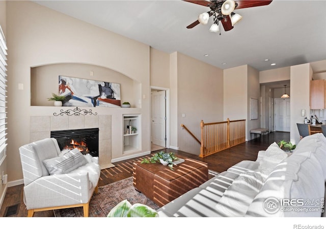 living room featuring built in shelves, ceiling fan, a tile fireplace, and dark hardwood / wood-style floors