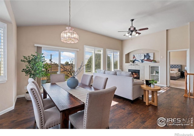 dining space featuring ceiling fan with notable chandelier, a tiled fireplace, lofted ceiling, and dark hardwood / wood-style floors