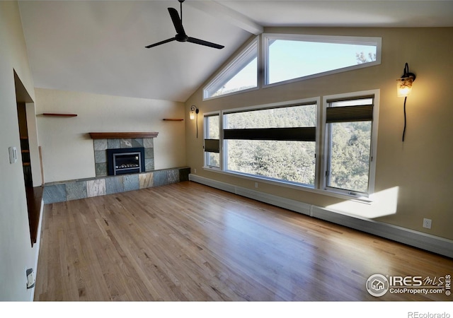 unfurnished living room with lofted ceiling with beams, a tiled fireplace, ceiling fan, and light hardwood / wood-style flooring