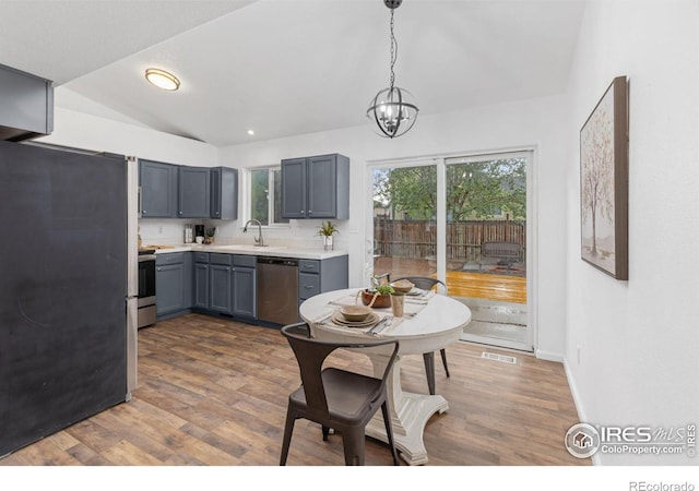 kitchen with appliances with stainless steel finishes, sink, hanging light fixtures, dark hardwood / wood-style floors, and vaulted ceiling