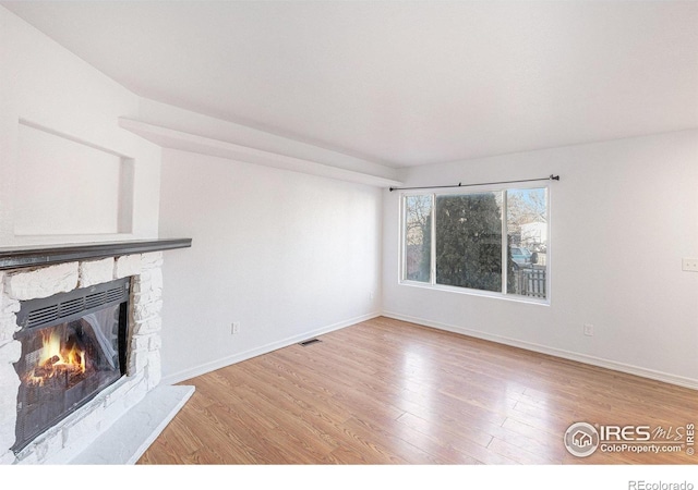 unfurnished living room featuring wood-type flooring and a stone fireplace