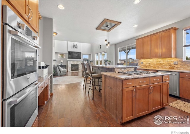 kitchen with pendant lighting, a center island, a kitchen bar, a stone fireplace, and stainless steel appliances