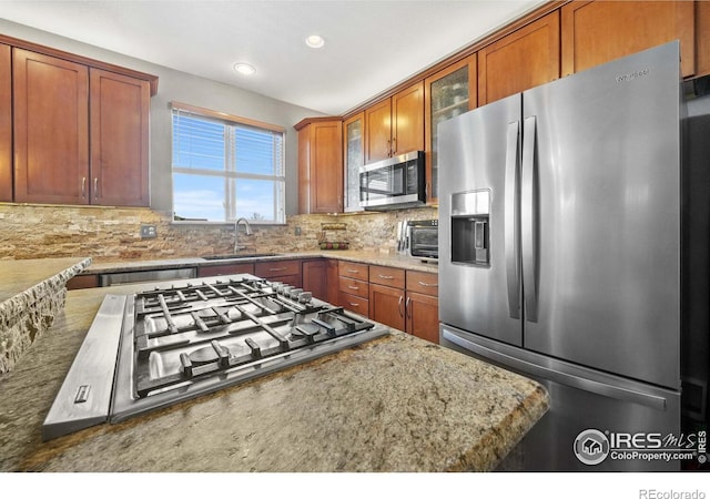 kitchen with light stone countertops, appliances with stainless steel finishes, sink, and tasteful backsplash