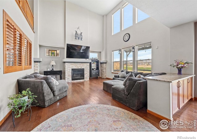 living room with a towering ceiling, hardwood / wood-style flooring, and a stone fireplace