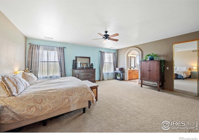 carpeted bedroom featuring ceiling fan, connected bathroom, and multiple windows