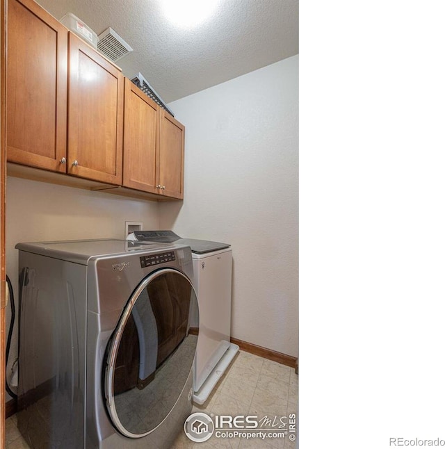 washroom featuring a textured ceiling, cabinets, and washing machine and clothes dryer